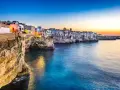 Solnedgång över Polignano a Mare, en pittoresk kuststad i Puglia, Italien. Vita hus klättrar på klipporna ovanför det turkosblå havet.