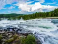 Vattenfall i Luleå med forsande vatten, grönskande skog och en blå himmel med vita moln.
