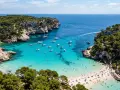 Vacker vik med turkost vatten, båtar och solande människor. En idyllisk plats där spanien vinter temperatur lockar besökare.