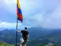 Vandrare med Colombias flagga på en bergstopp. Trots ryktet om att en resa till Colombia kan vara farligt, njuter han av den dramatiska utsikten.