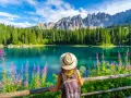 En kvinna med hatt och ryggsäck njuter av en vacker sommardag vid en turkos sjö i Dolomiterna.
