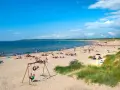 En solig strand i Halland med många badgäster, sanddyner och en gungställning.