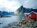 Två röda stugor vid en sjö i Norge, med dramatiska berg i bakgrunden. Perfekt för den som vill vandra i Norge.