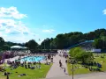 En solig dag vid en populär badplats i Stockholm. Människor solar, badar och njuter av sommaren på gräsmattor och i poolen.