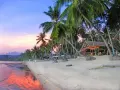 En vacker strand på Koh Samui, Thailand, med vajande palmer, en strandbar och ett hav som speglar den rosa solnedgången.