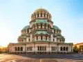 Imponerande kyrka med gröna kupoler och ett gyllene kors i Sofia, Bulgarien. En vacker syn i morgonsolen.