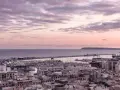 En vacker solnedgång över hamnen i Alicante i december. Molnen färgas i rosa och lila över havet och staden.