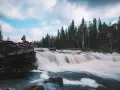 Person sitter på en klippa vid ett forsande vattenfall i Dalarna, ett perfekt utflyktsmål.