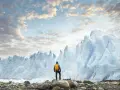 En person med gul ryggsäck står på stenar framför en enorm glaciär. Ett perfekt resmål i januari för den äventyrlige.