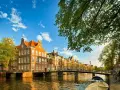 En vacker kanalvy i Amsterdam med klassiska hus, broar och båtar. Perfekt för din amsterdam reseguide.