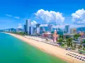 En vidsträckt strand med turkost vatten och en stadssilhuett i bakgrunden. Nha Trang beach är en populär destination.