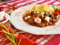 En smak av mat i Budapest: mustig gulasch med nokedli, garnerad med gräddfil och en rosmarinkvist. En röd chili och en tomatblomma fulländar upplägget.