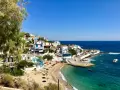 En pittoresk kustby på Ikaria, Grekland, med vita hus, en sandstrand och turkost vatten.
