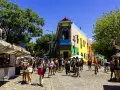 Färgglada hus och marknadsstånd i Buenos Aires. En livlig gata med människor som njuter av solen.