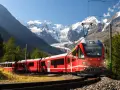 Ett rött tåg slingrar sig fram genom ett dramatiskt alplandskap med snöklädda berg. Kanske är det ett tåg till Italien, med hisnande vyer längs vägen.