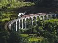Ångloket på Glenfinnanviadukten i Skottland, som påminner om Harry Potter tåg skottland, ångar fram över den gröna dalen.