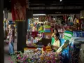 En livlig marknad i Bangkok med försäljare och kunder bland färgglada varor och blommor.