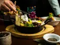 En hand dekorerar en mustig gryta med kött, potatis och blommor. En utsökt rätt som påminner om kanadensiskt kök.