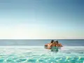 Ett par kysser varandra i en infinitypool med havet i bakgrunden. Perfekt för romantiska resmål.