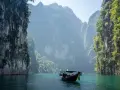 En båt färdas på turkost vatten genom dramatiska kalkstensklippor i Khao Sok nationalpark.