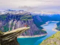 Två personer står på Trolltunga, en klippavsats i Norge, med en fantastisk utsikt över bergen och naturen.