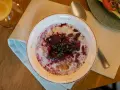 En skål med gröt toppad med bär och russin, en del av en kroatisk frukost. Bredvid syns en smörgås och ett glas juice.