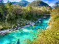 Turquoise flod genom bergig skog i Slovenien. En bro syns i fjärran.