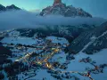 En snötäckt by i Italien på vintern, upplyst av tusentals ljus. Majestätiska berg reser sig bakom, inbäddade i dimma.
