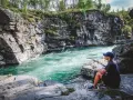 En person sitter vid en forsande älv i en ravin. En perfekt hemester i Sverige.