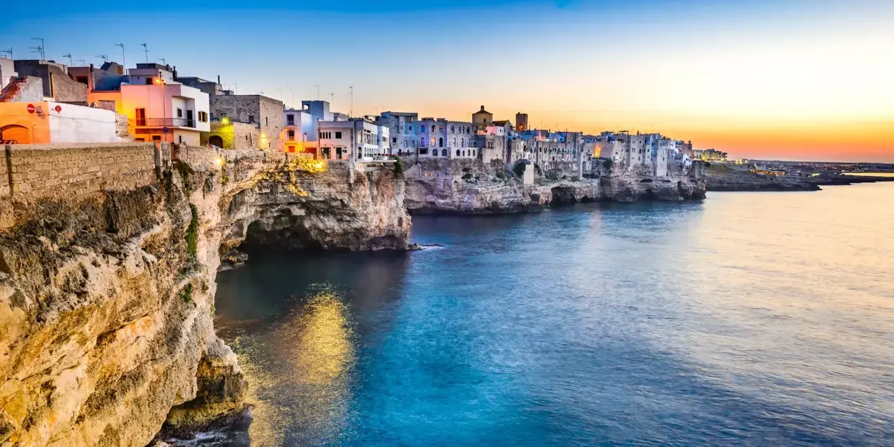 Solnedgång över Polignano a Mare, en pittoresk kuststad i Puglia, Italien. Vita hus klättrar på klipporna ovanför det turkosblå havet.