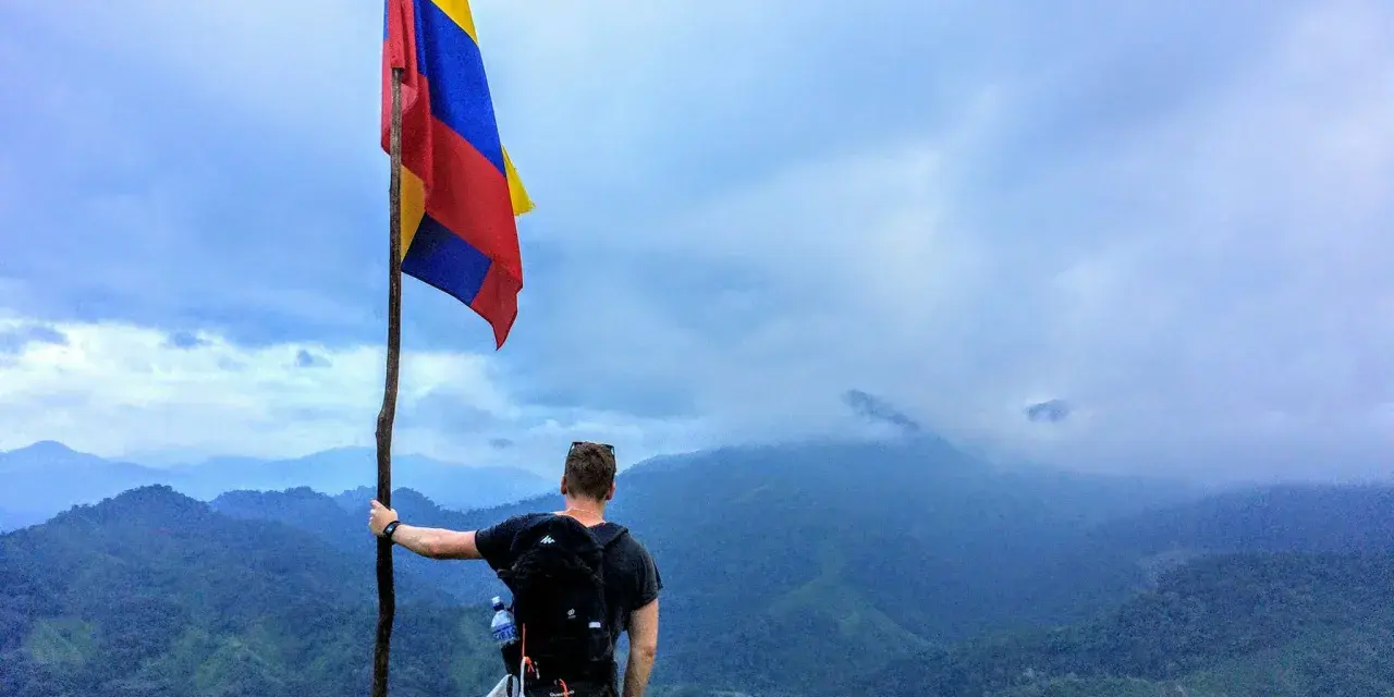 Vandrare med Colombias flagga på en bergstopp. Trots ryktet om att en resa till Colombia kan vara farligt, njuter han av den dramatiska utsikten.