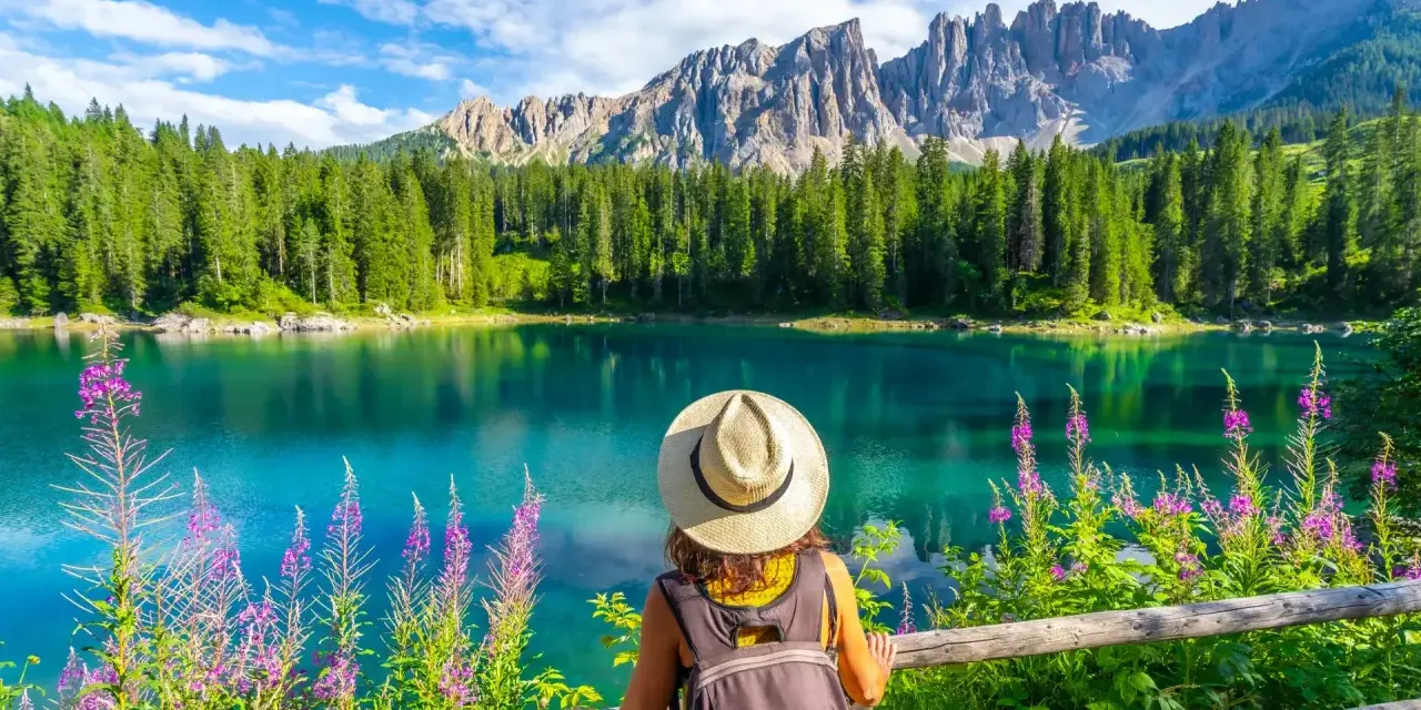 En kvinna med hatt och ryggsäck njuter av en vacker sommardag vid en turkos sjö i Dolomiterna.