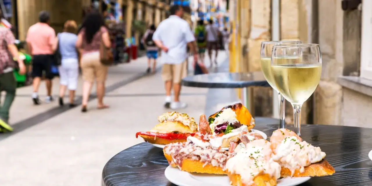 Tapas och vin på en uteservering i San Sebastián. Folk promenerar förbi på den livliga gatan.