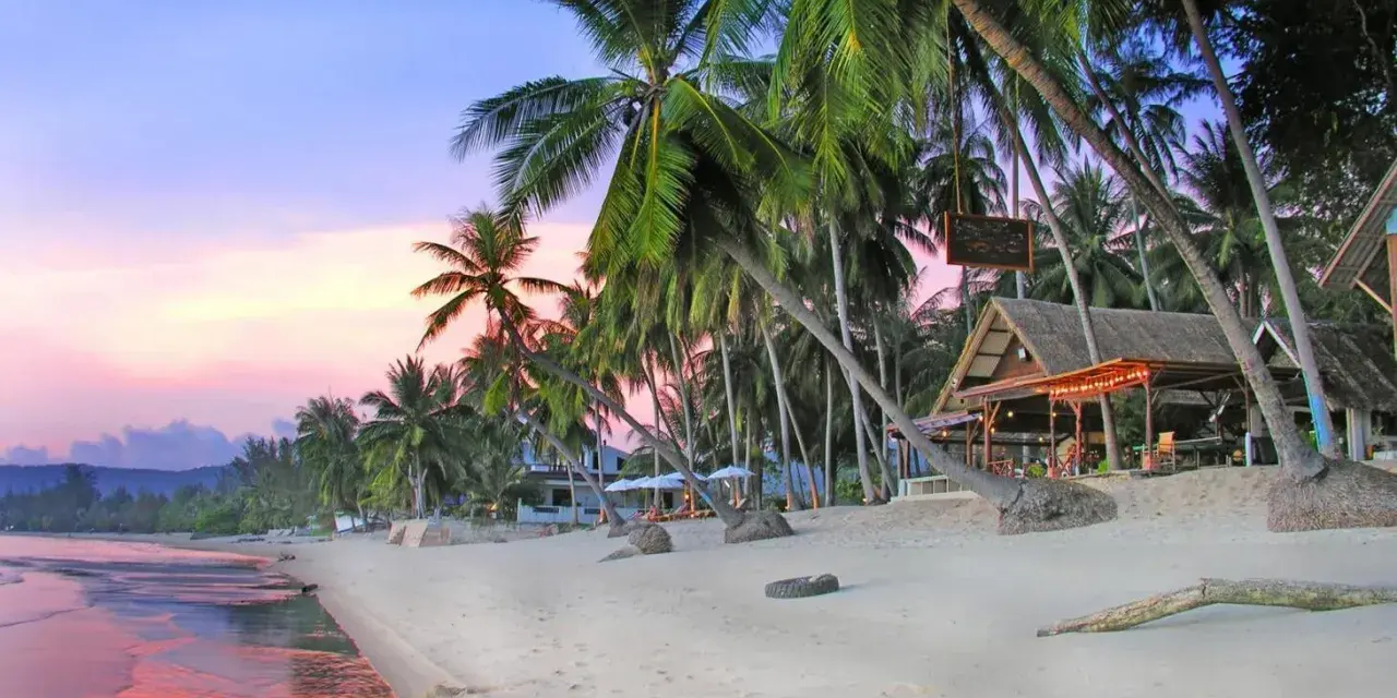 En vacker strand på Koh Samui, Thailand, med vajande palmer, en strandbar och ett hav som speglar den rosa solnedgången.
