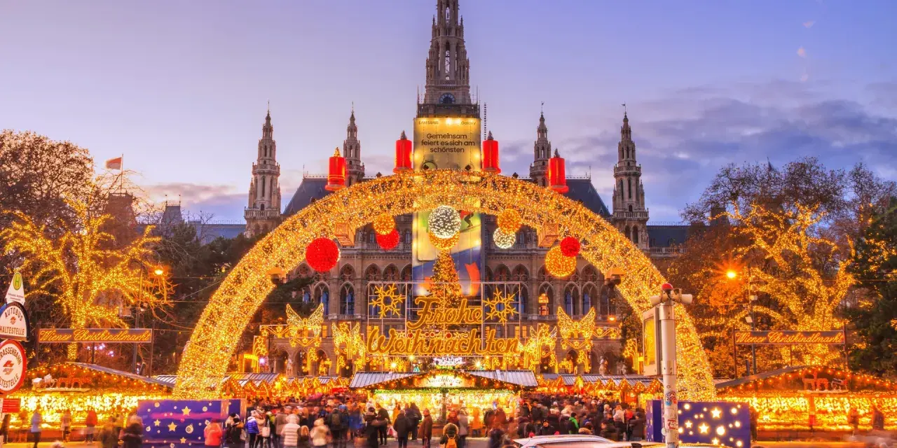En magisk julmarknad i Wien, med Rådhuset i bakgrunden, gnistrar av tusentals ljus. En båge av gyllene ljusslingor välkomnar besökare till den livliga julmarknaden.