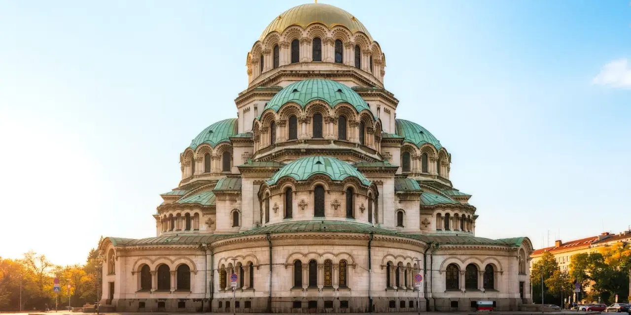 Imponerande kyrka med gröna kupoler och ett gyllene kors i Sofia, Bulgarien. En vacker syn i morgonsolen.