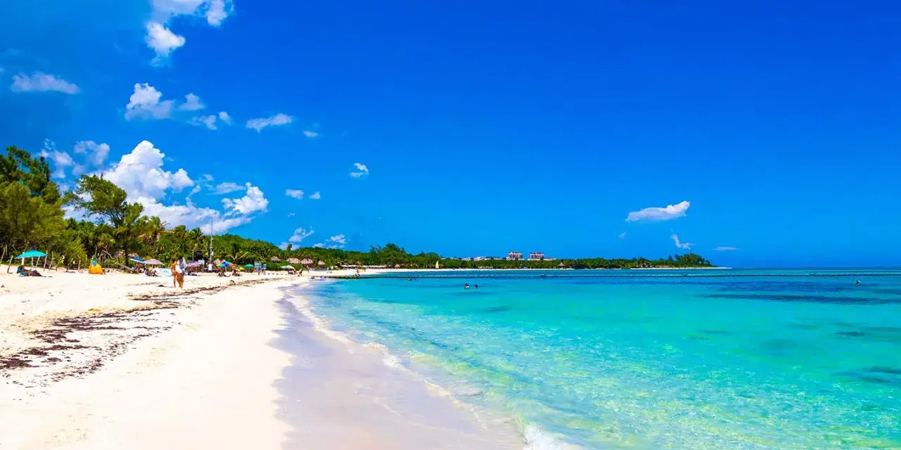 Vacker strand med turkost vatten och vita moln. Trots den idylliska vyn, kan Playa del Carmen vara farligt.