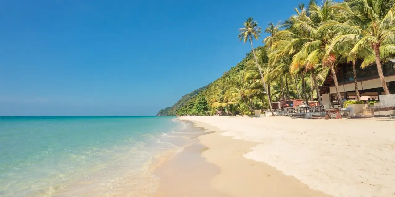 En strand på Ko Chang med palmer, turkost vatten och en byggnad.