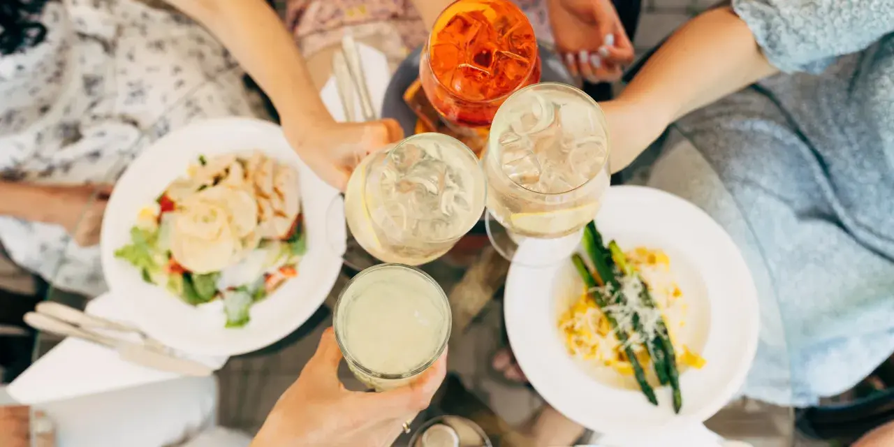 Vänner skålar med drinkar och njuter av en härlig milano mat-upplevelse med sallad och pasta med sparris.