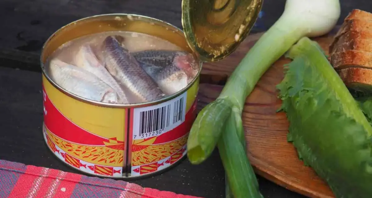 En burk med sill, en klassisk del av **comida tipica sueca**, ligger bredvid färska grönsaker och bröd.