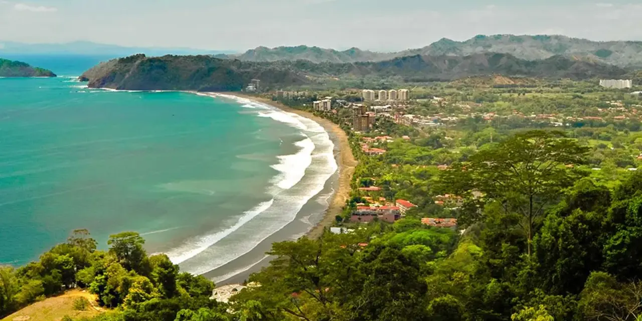Vacker kustlinje med turkost hav, vågor som slår mot en sandstrand och frodig grönska som omger en stad. En dröm om en costa rica strand.