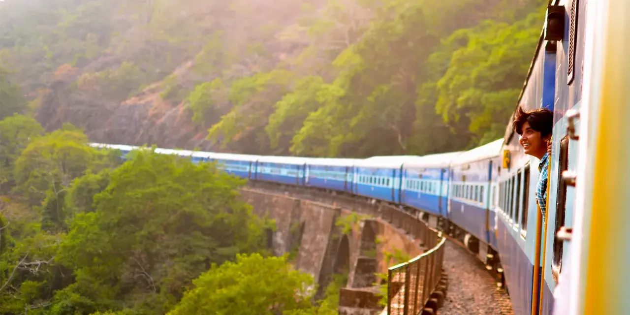 Ung man ler från tågfönstret på en resa genom grönskande landskap. Bra interrail tips för äventyrliga resor!