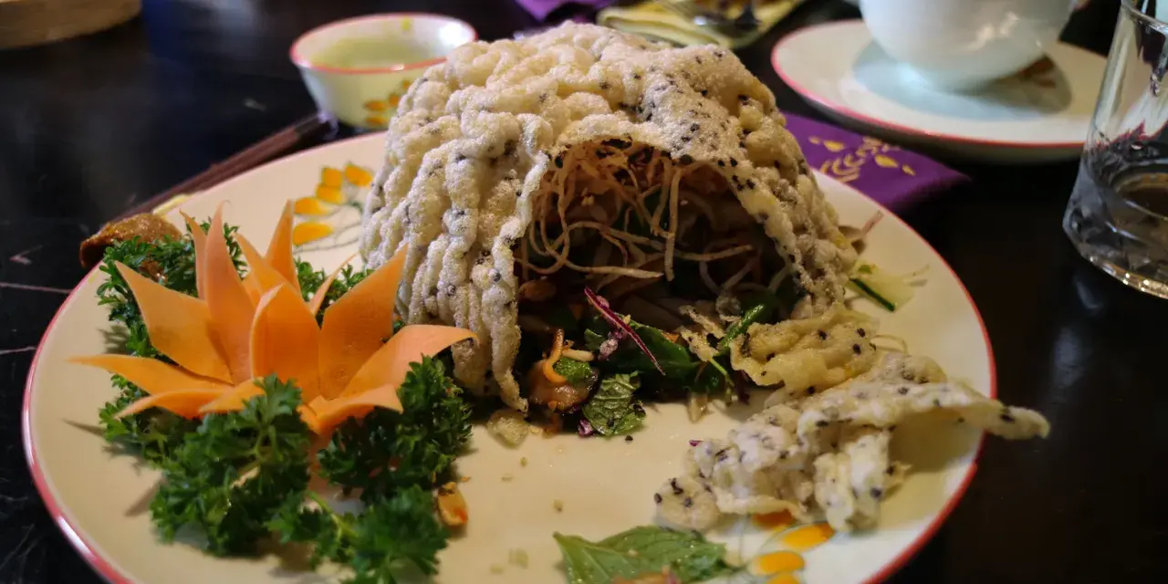 En vacker vietnamesisk maträtt med krispig rispapperstäckt sallad, dekorerad med morotsblomma och örter.