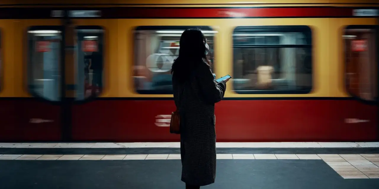 Kvinna med mobil på perrongen i Berlin, en gul och röd tunnelbanevagn susar förbi. Perfekt för din berlin reseguide.