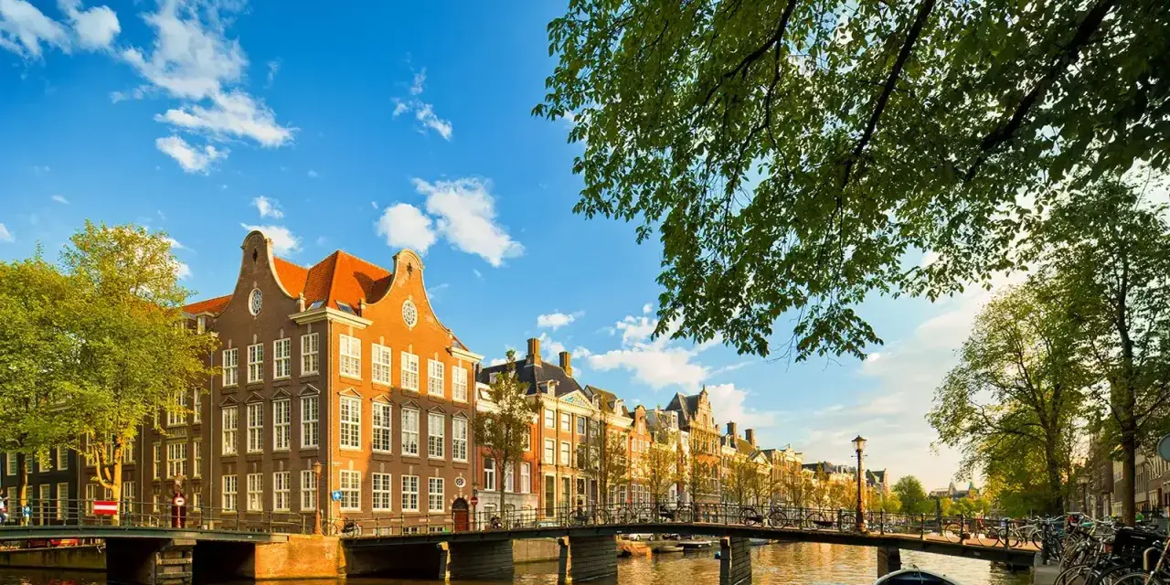 En vacker kanalvy i Amsterdam med klassiska hus, broar och båtar. Perfekt för din amsterdam reseguide.
