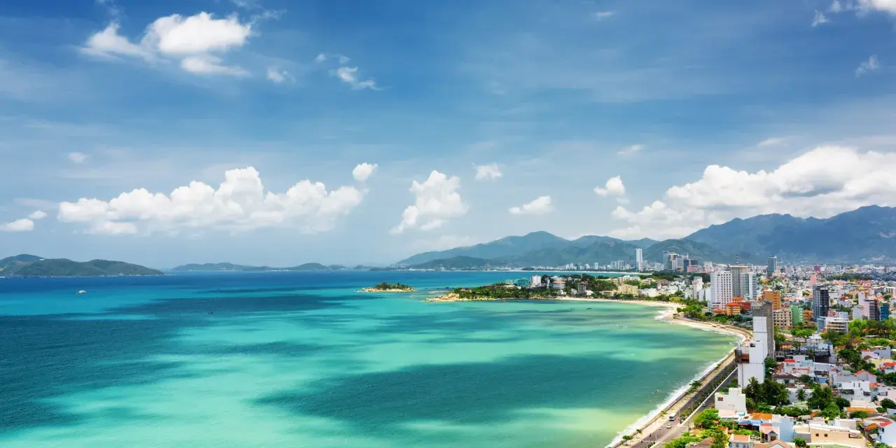Vacker vy över Nha Trang, Vietnam, med turkost vatten, gröna kullar och en stad vid kusten under en blå himmel med moln.