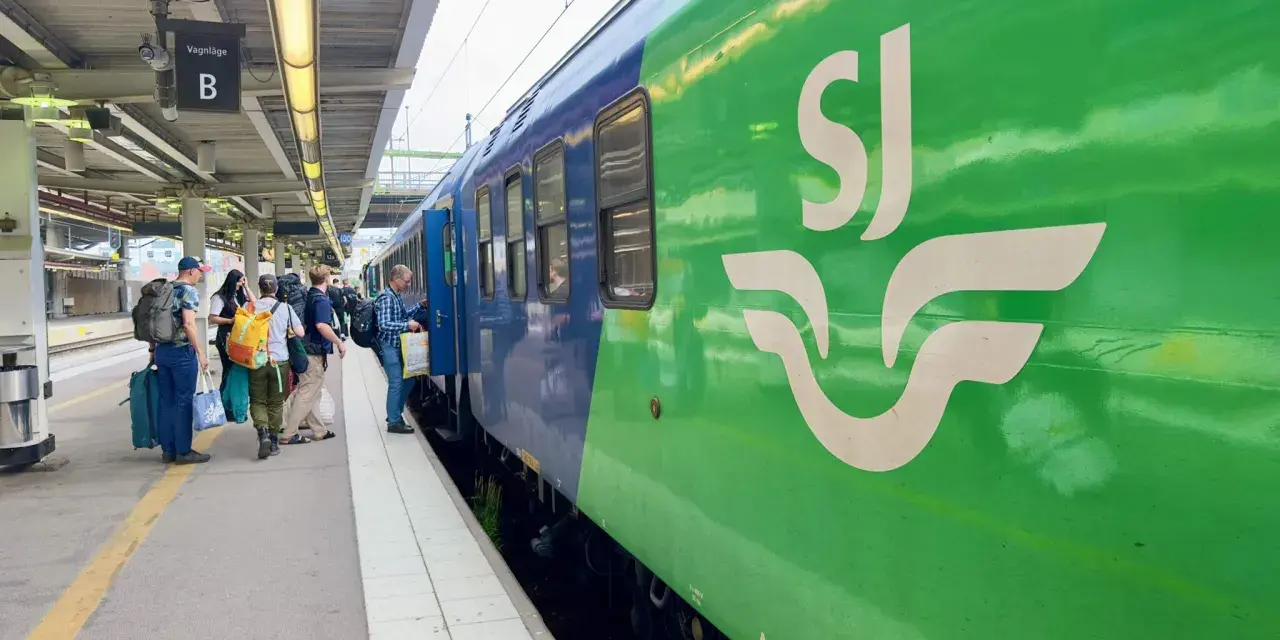 Folk väntar på perrongen vid vagnhall B. Ett grönt SJ-tåg står redo för resan, kanske till och med ett tåg till London.