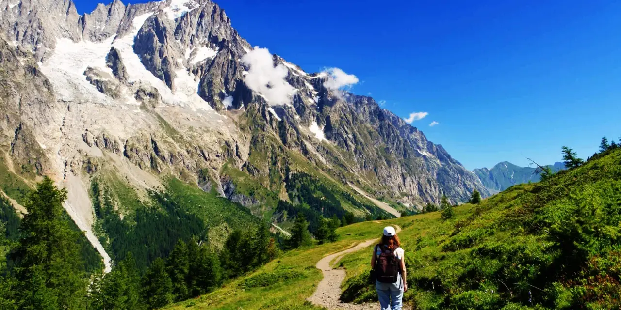En person vandrar på en stig i Chamonix med majestätiska berg och en glaciär i bakgrunden.