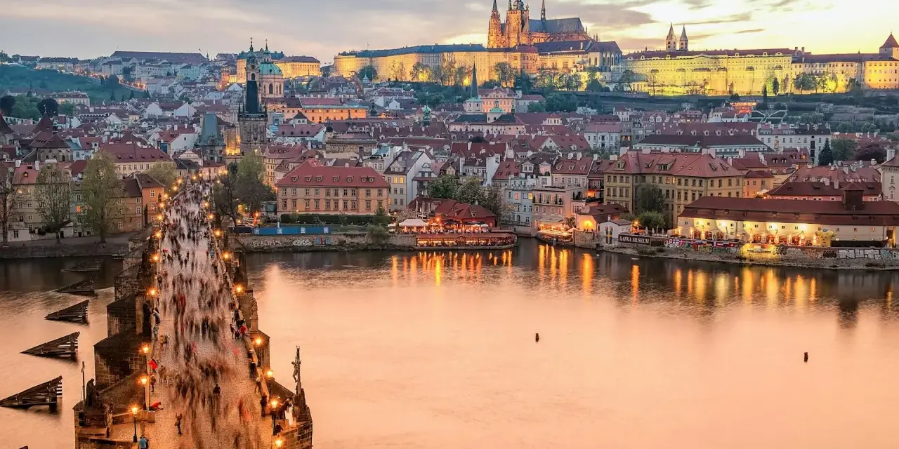 En livlig kväll på Karlsbron i Prag, med tusentals besökare som promenerar mot slottet. En perfekt vy för den som tar tåg till Prag.