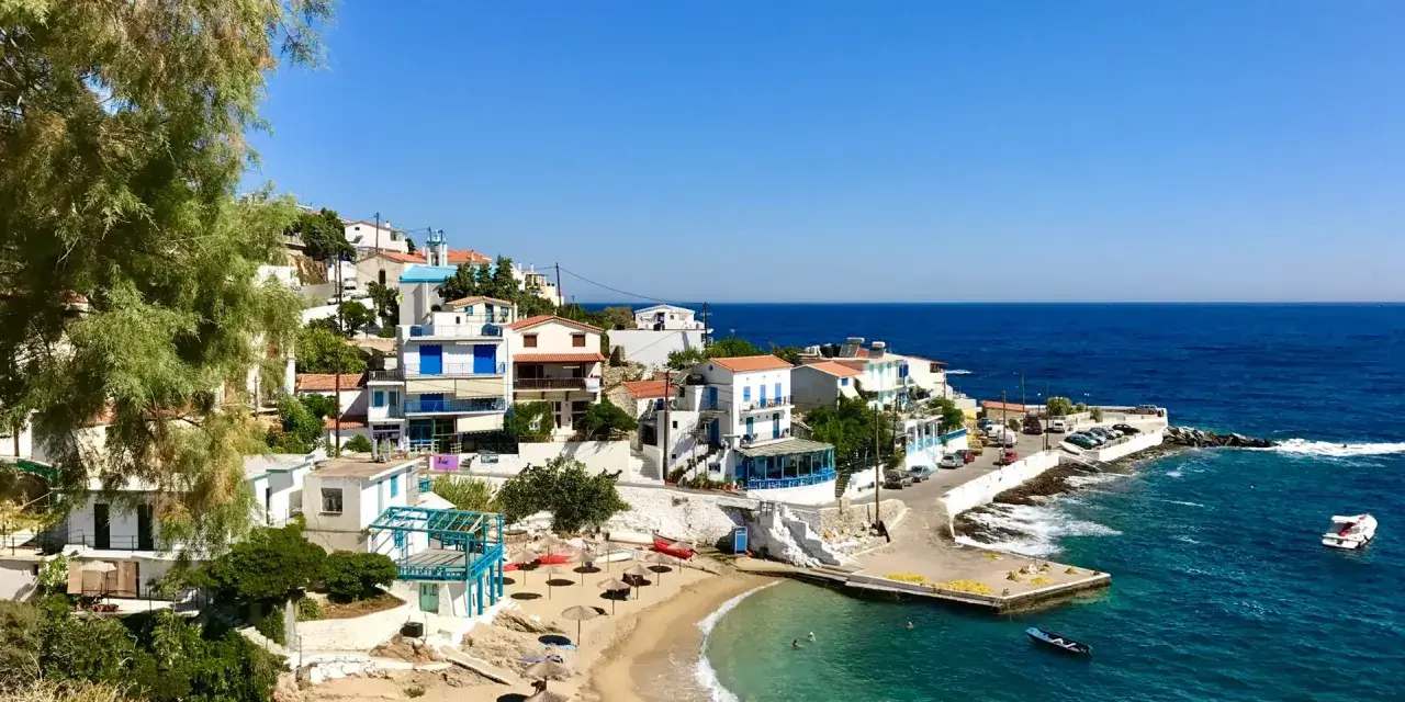 En pittoresk kustby på Ikaria, Grekland, med vita hus, en sandstrand och turkost vatten.
